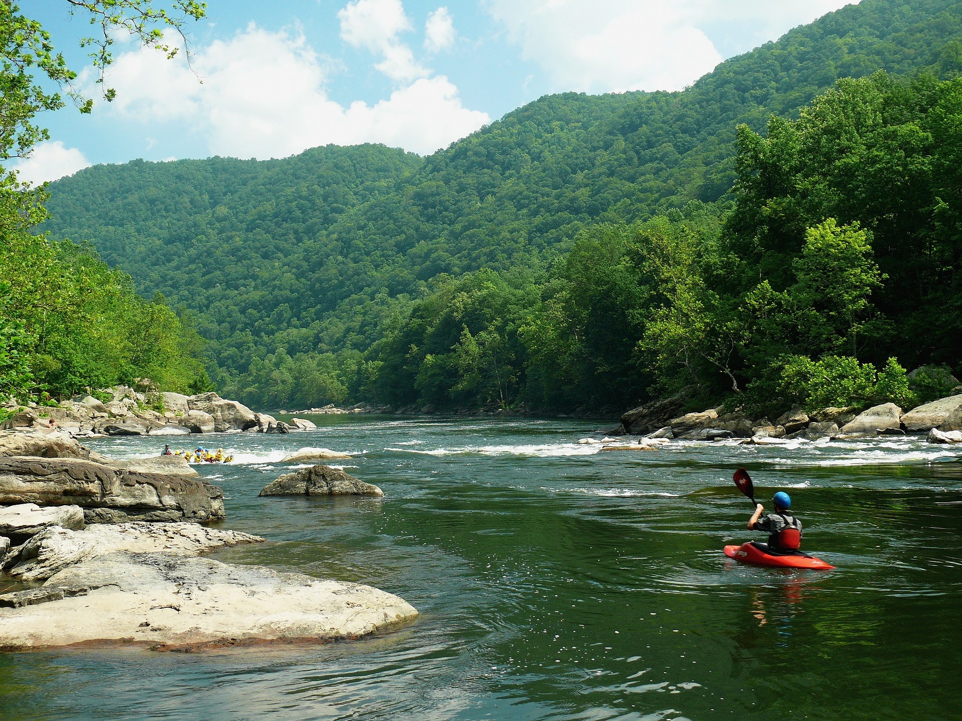 Person kayaking in river surrounded by mountains