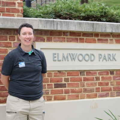 Young woman posing in front of brick Elmwood Park sign