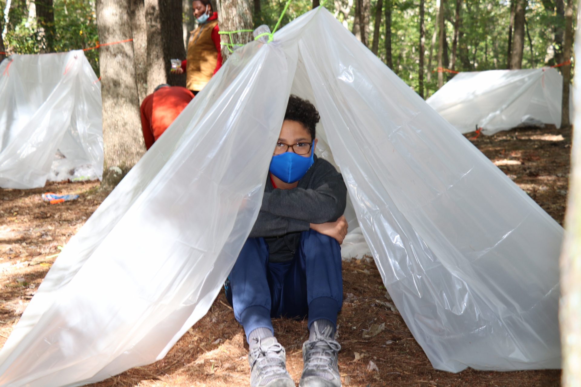 Kid wearing mask huddled beneath plastic tent