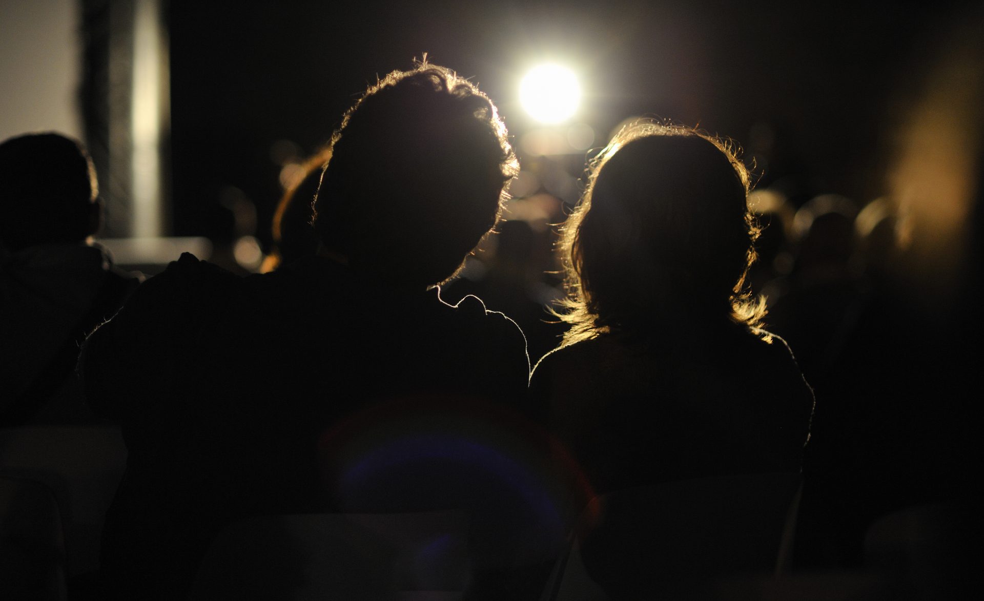 The silhouette of the back of two people watching an outdoor movie