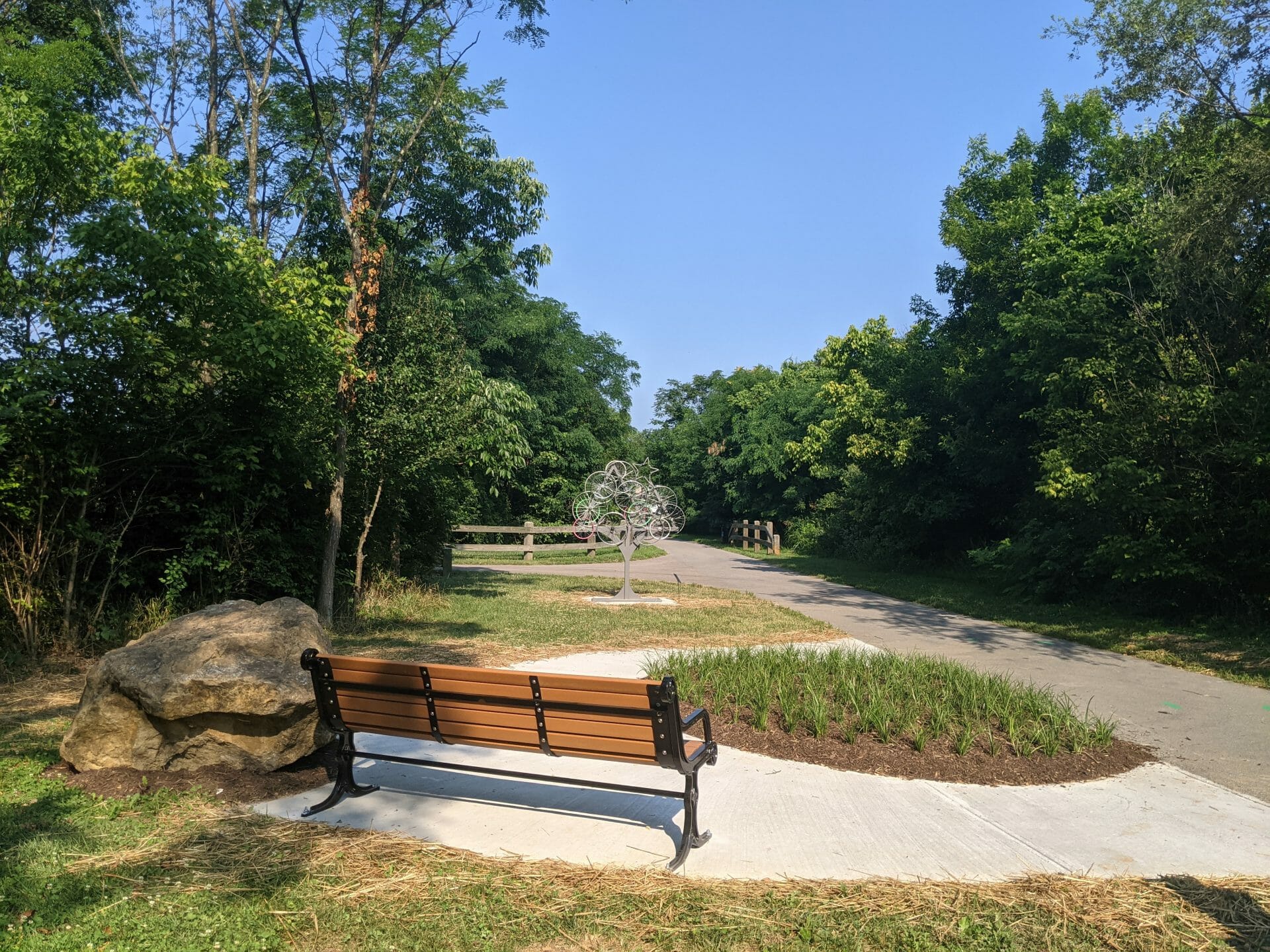 Plaza along the greenway path with a bench facing a sculpture