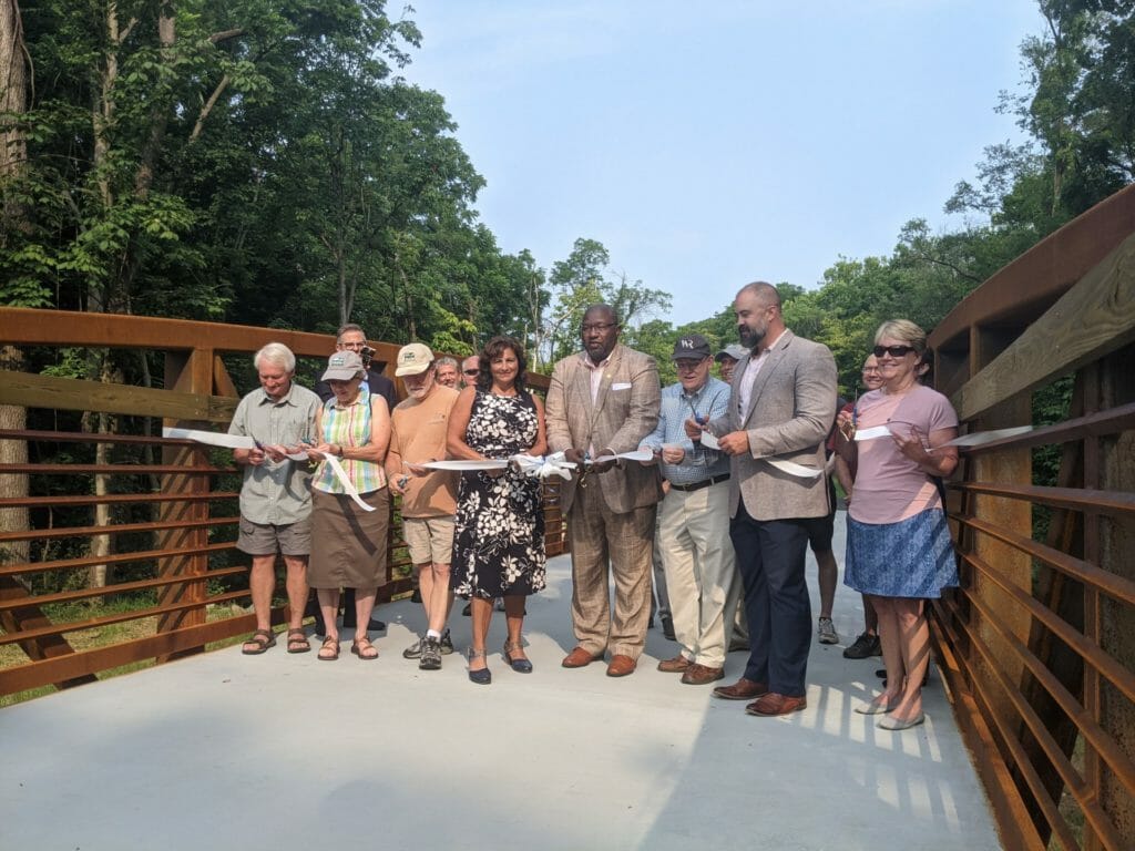Group of several people gathered, cutting the ribbon on a new bridge