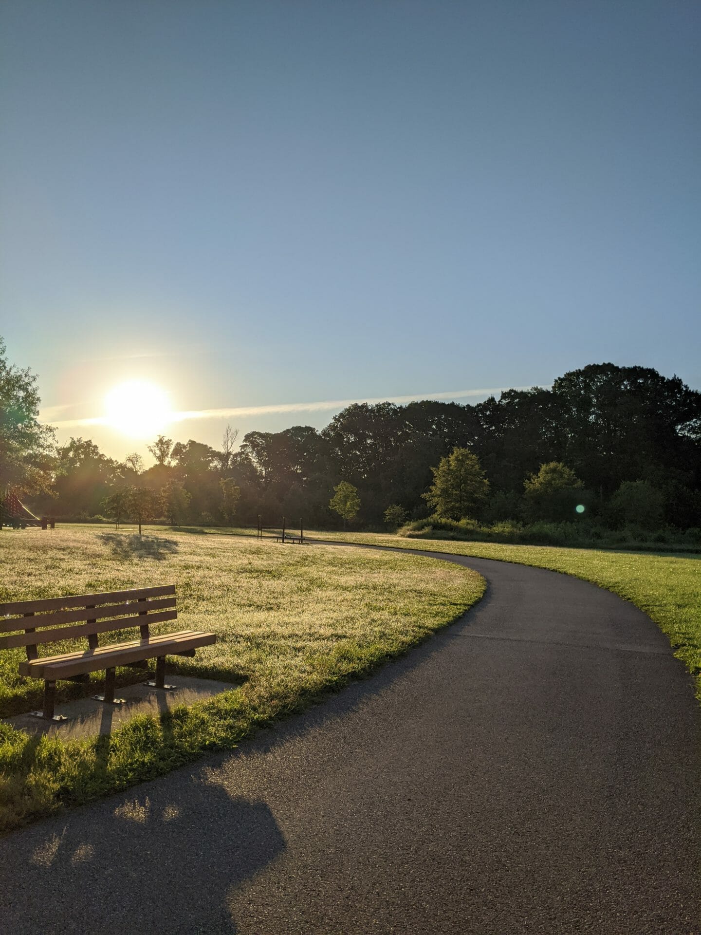 Paved path at sunrise with a bench next to it