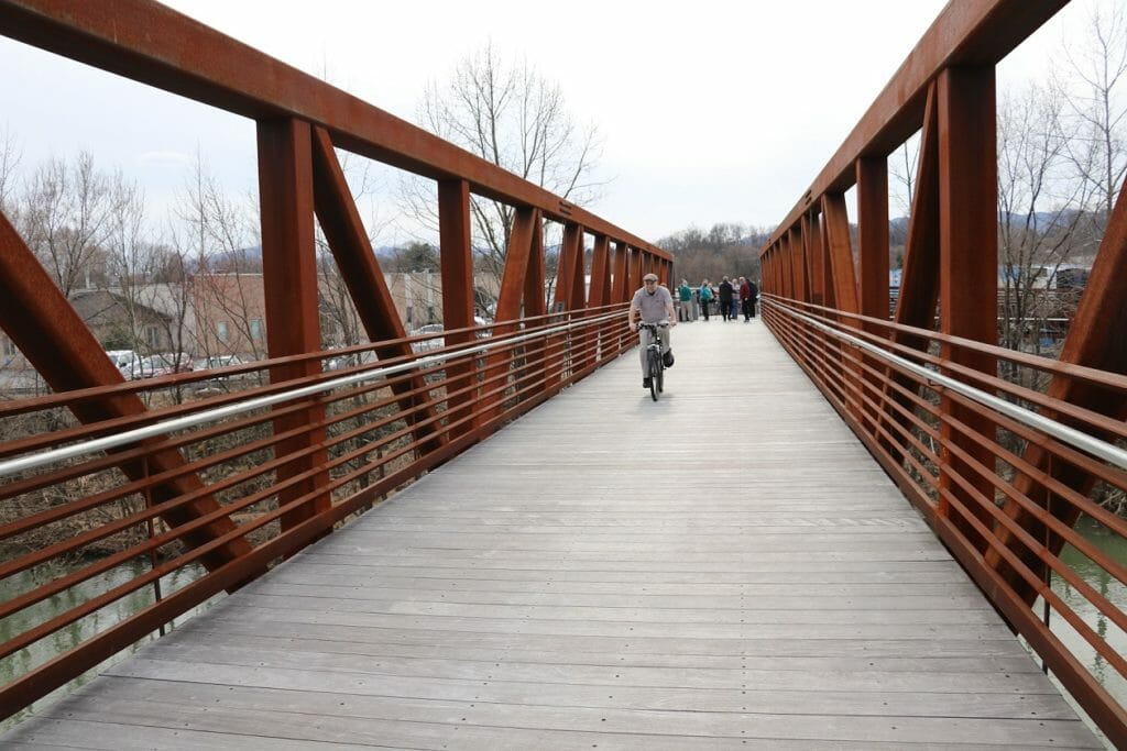 Industrial pedestrian bridge with white man in grey coat riding a bike over it.