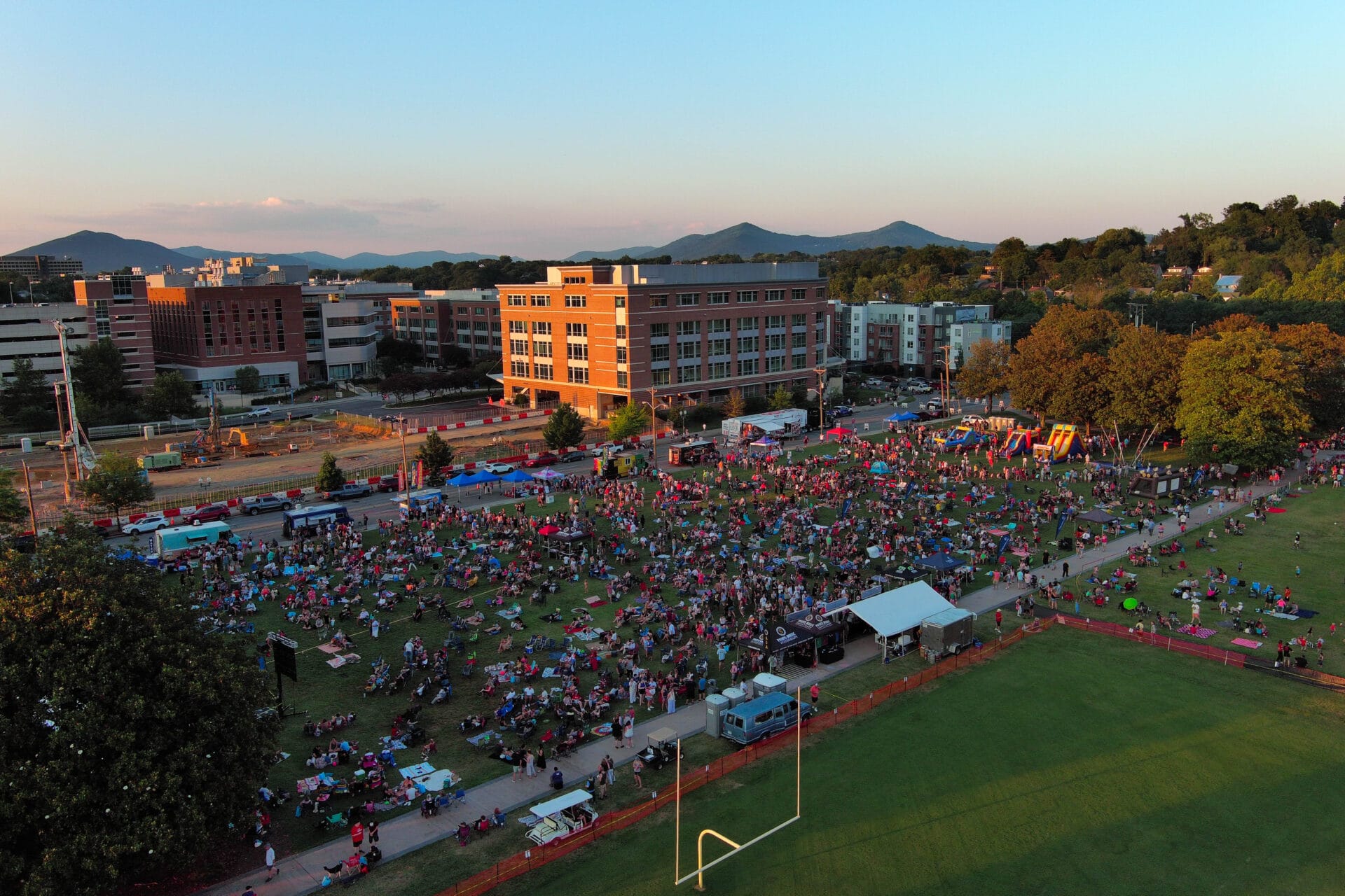 Freedom Festival & Fireworks Aerial view of a large crowd at a festival in a park with music stage, bounce houses, food trucks.