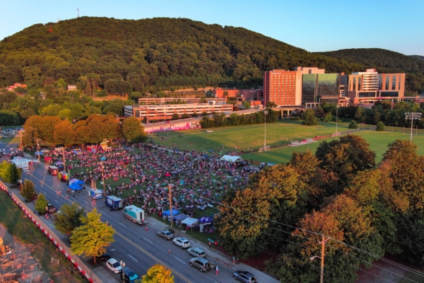 Freedom Festival & Fireworks Aerial view of a large crowd at a festival in a park with music stage, bounce houses, food trucks.