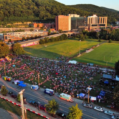 Aerial view of large crowd in a park with food trucks, stage, and bounce houses