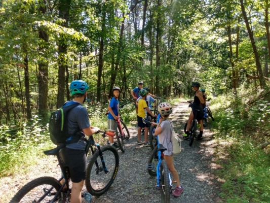 PLAYsummercamp 05 A counselor and campers prepare to mountain bike on a forested trail.