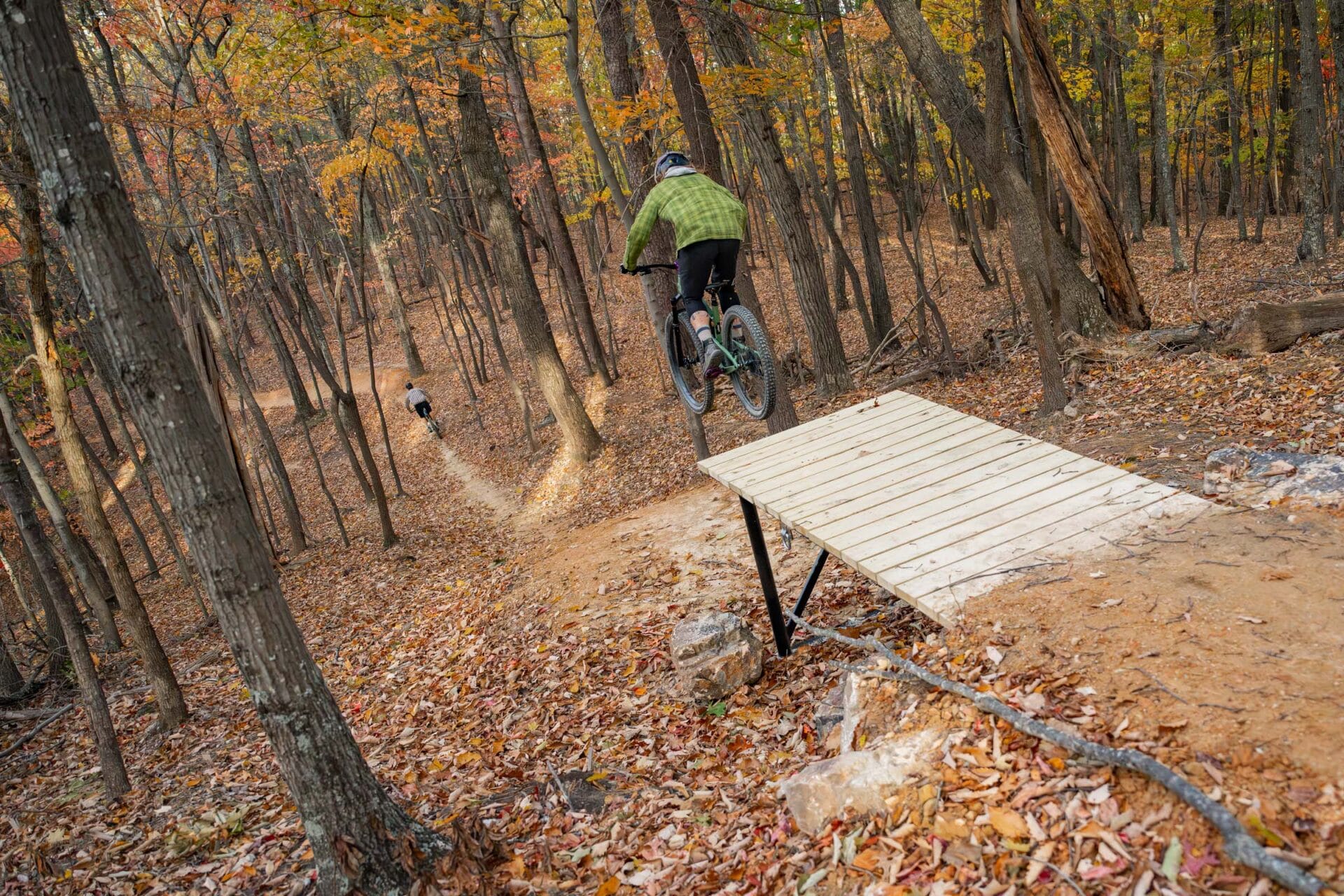 A biker rides off a wooden ramp jump feature on downhill mountain bike trails on Mill Mountain.