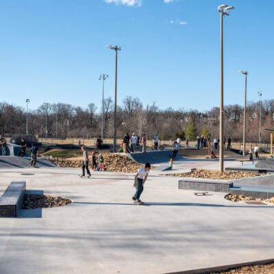 A busy skatepark on a sunny day with skateboarders, bikes, and other users.