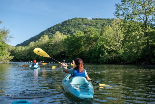 RoanokeRiverEveningKayak web 834 A woman paddles a kayak on a river with Mill Mountain and the Roanoke Star in the distance.