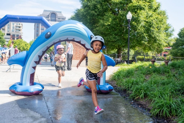 Tiny Tot Tri Two girls run through a sprinkler as part of a 'triathlon' event for toddlers and small children in a city park.