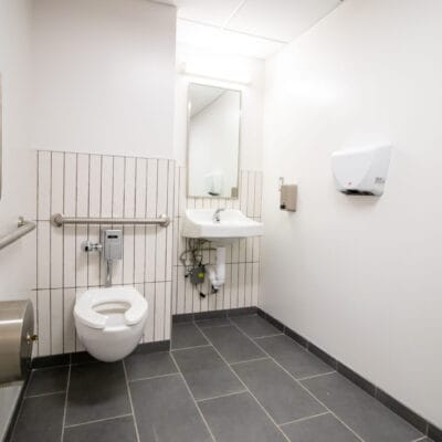 Restroom with ADA toilet, sink, mirror, and hand dryer.
