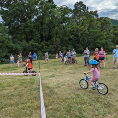PXL 20240503 214649901.MP A group of young mountain bikers compete in a race at a city park while their parents cheer them on.