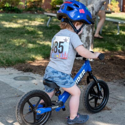 TinyTotTri26 852web A toddler on a balance bike rides beside their parent while competing in a 'triathlon' event for toddlers.