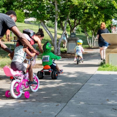 TinyTotTri26 876web A group of children helped by their parents ride bikes as part of a 'triathlon' event for toddlers and small children.
