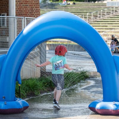 TinyTotTri26 889web A child run through a sprinkler as part of a 'triathlon' event for toddlers and small children in a city park.